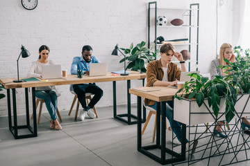 multicultural business colleagues sitting at table and working on laptops in modern office