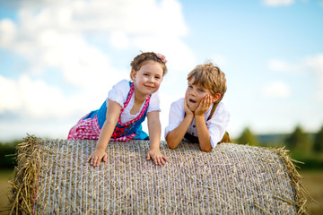 Wall Mural - Two kids, boy and girl in traditional Bavarian costumes in wheat field with hay bales