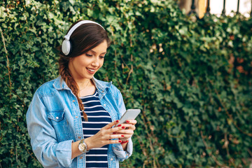 Wall Mural - Young woman listens to music via headphones and smartphone in the city