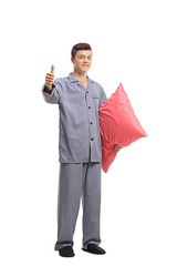 Wall Mural - Teenage boy in pajamas holding a pillow and making a thumb up gesture