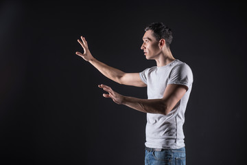 Computer programming. Nice handsome smart man standing against black background and looking at the screen while using sensory computers for work