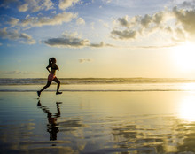 Silhouette Of Young Asian Sport Runner Woman In Running Workout Training At Sunset Beach With Orange Sunlight Reflection On The Sea Water