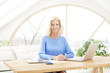 © sepy - Businesswoman working from home. Portrait of smiling blond businesswoman writing something and working on laptop while sitting at desk.