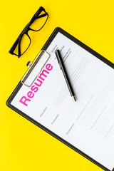 Poster - Looking for work concept. Resume on pad near pen and glasses on yellow background top view