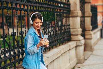 Wall Mural - Young woman listens to music via headphones and smartphone in the city