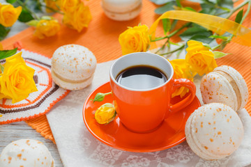 Wall Mural - Orange cup of black coffee, yellow roses flowers and sweet pastel french macaroons