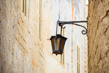 Wall Mural - Malta, Mdina. Old lantern lamp in the medieval city with the narrow streets and houses limestone facades