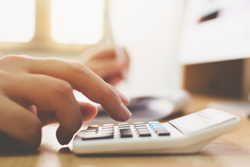 Close up hand of businessman doing financial accountant and using calculator with computer desktop