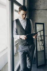 Portret of young beautiful young business man operating with tablet leaning against the window.