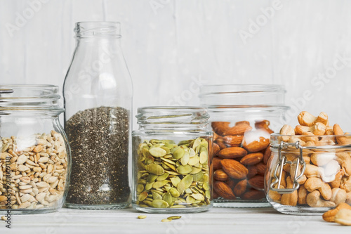Fotomural Various nuts and seeds in glass jars over white wooden table against white background