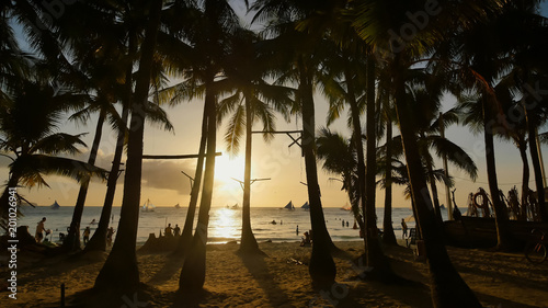 Beach With Silhouettes Of Tourists Among Palm Trees On The