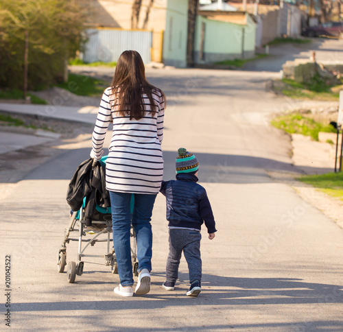 Fotografia, Obraz A woman with a baby and a stroller walk along the road