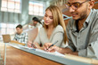© Seventyfour - Multi-ethnic group of students sitting at desk in lecture hall of modern college and writing, focus on young Middle-Eastern man wearing glasses, copy space