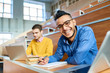 Portrait of two students sitting at desks in modern auditorium at college and preparing for class, focus on young Middle-Eastern man looking at camera and smiling, copy space