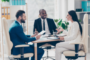 Wall Mural - Attractive modern stylish elegant employees talking about new strategy, trying to find resolution, sitting in work station on armchairs, gesturing with hands, holding tablet, clipboard, wearing suits