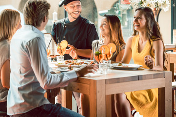 Experienced chef smiling congratulated for the delicious food by four young people at the table of a trendy exclusive restaurant