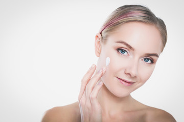 Portrait of happy smiling beautiful young woman touching skin or applying cream, isolated over white background