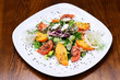 © Volodymyr - Salad served in white plate, dark wooden background. Restaurant dish concept. Dish in restaurant salad with tomatoes, arugula, persimmon, onions, lettuce, radicchio, feta cheese with spices, sesame.