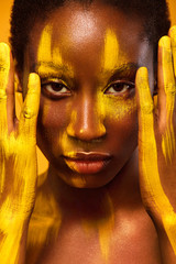 Wall Mural - Cheerful young african woman with yellow spring makeup on her eyes. Female model laughing against yellow summer background.