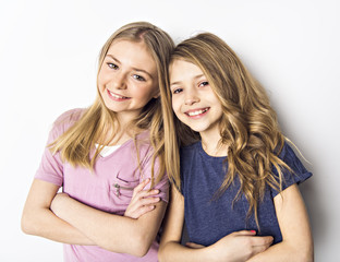 Portrait of two little friend girl close to a white wall