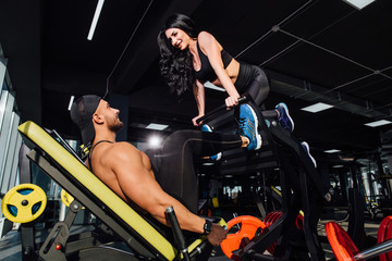 Personal trainer helping a men working out on leg press machine in gym