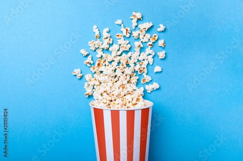 Fotografía Spilled popcorn and paper bucket in red strip on blue background