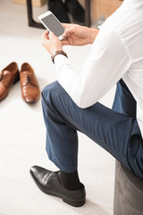 Poster - Man using smartphone while trying on new shoes indoors