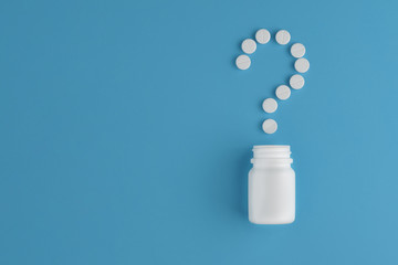 Pharmaceutical pills and a bottle on a blue background. Concept question mark