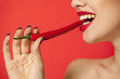 Young sexy woman biting a chili pepper on red background