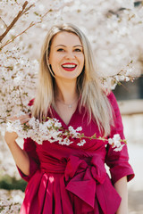 Wall Mural - outdoor portrait of beautiful blond woman wearing pink dress, posing in spring blooming flowers