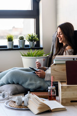 Wall Mural - Beautiful young woman reading e book reader at home surrounded by books