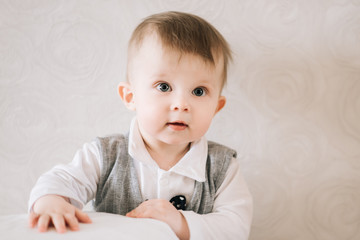 Wall Mural - Happy cute boy in a gentleman's suit stands near the support on a light background, trying to get up, learning to walk.