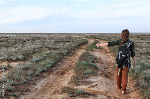 Fotografía Girl hitchhiker on a country dirt road in steppe in the evening