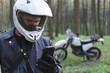 © Sergey - classic enduro motorcycle off road in spring forest, man in a stylish leather jacket uses a smartphone, Motorcyclist gear, A motorcycle driver looks, concept, active lifestyle