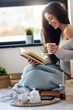 © lordn - Beautiful young woman reading a book, enjoying by the window in modern apartment.