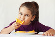 © kaganskaya115 - little cute child girl dressed in a purple blouse holding an orange and eating off a piece of orange