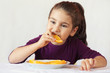 © kaganskaya115 - little cute child girl dressed in a purple blouse holding an orange and eating off a piece of orange