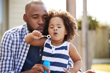 Wall Mural - Young black father and daughter blowing bubbles outside