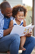 © Monkey Business - Young black father and daughter reading book outside