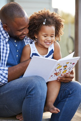 Wall Mural - Young black father and daughter reading book outside