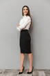© Drobot Dean - Full length portrait of successful young woman 20s with long brown hair in business wear smiling at camera and keeping arms crossed, isolated over white background