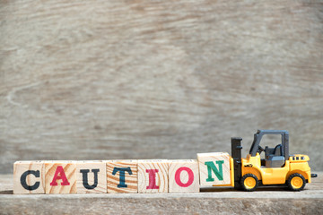 Poster - Toy forklift hold letter block N to complete word caution on wood background