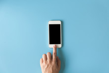 Top View Of  Hand Touching Smartphone On The Blue Pastel Color Background.
