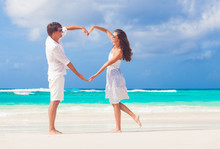 Young Happy Couple In White Making Heart Shape On Tropical Beach. Honeymoon