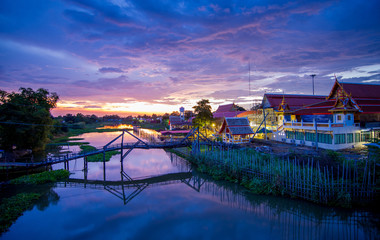Wall Mural - The view of countryside among natural small creek with old temple, old wooden bridge and beautiful sky during sunset in Suphanburi, Thailand.