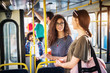 © dusanpetkovic1 - Two beautiful young women are drinking coffee and having a chat while standing in the bus and holding onto the bars.