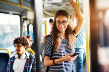 Young Gorgeous Cheerful Woman Is Standing On The Bus Using The Phone And Smiling.