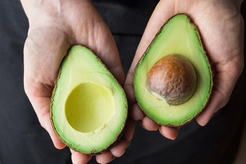 Young Caucasian Woman in Black Apron Holding in Hands Ripe Beautiful Halved Organic Australian Avocado with Pit. Healthy Lifestyle Vegan Vitamin E Oil. Creative Minimalist Food Poster Banner. KInfolk