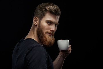 Wall Mural - Young happy bearded man drinking morning fresh expresso coffee Caucasian handsome male business professional having coffee indoors close up studio portrait Side view portrait of stylish hairstyle man.