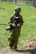 © Natali - Boy in the camouflage holds a paintball gun  in one hand and protective helmet , standing on the field with group of players on the background